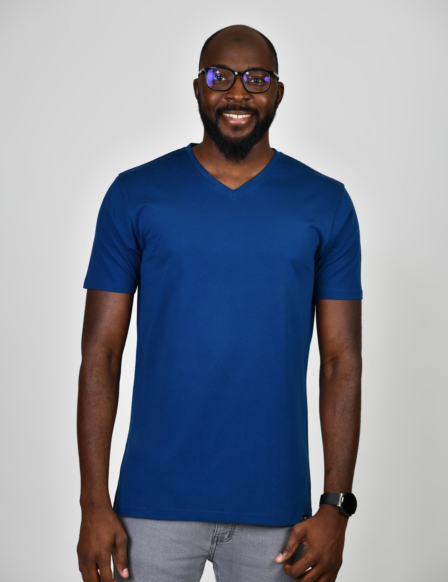 A tall and slim man in the studio standing in front of a light background. The smiling model is wearing an extra long slim navy blue v-neck t-shirt in a size large. The tall navy blue v-neck t-shirt features a 3" longer body, 100% organic cotton, and is soft & preshrunk. The navy blue v-neck t-shirt is ideal for tall slim men 6'2"+.