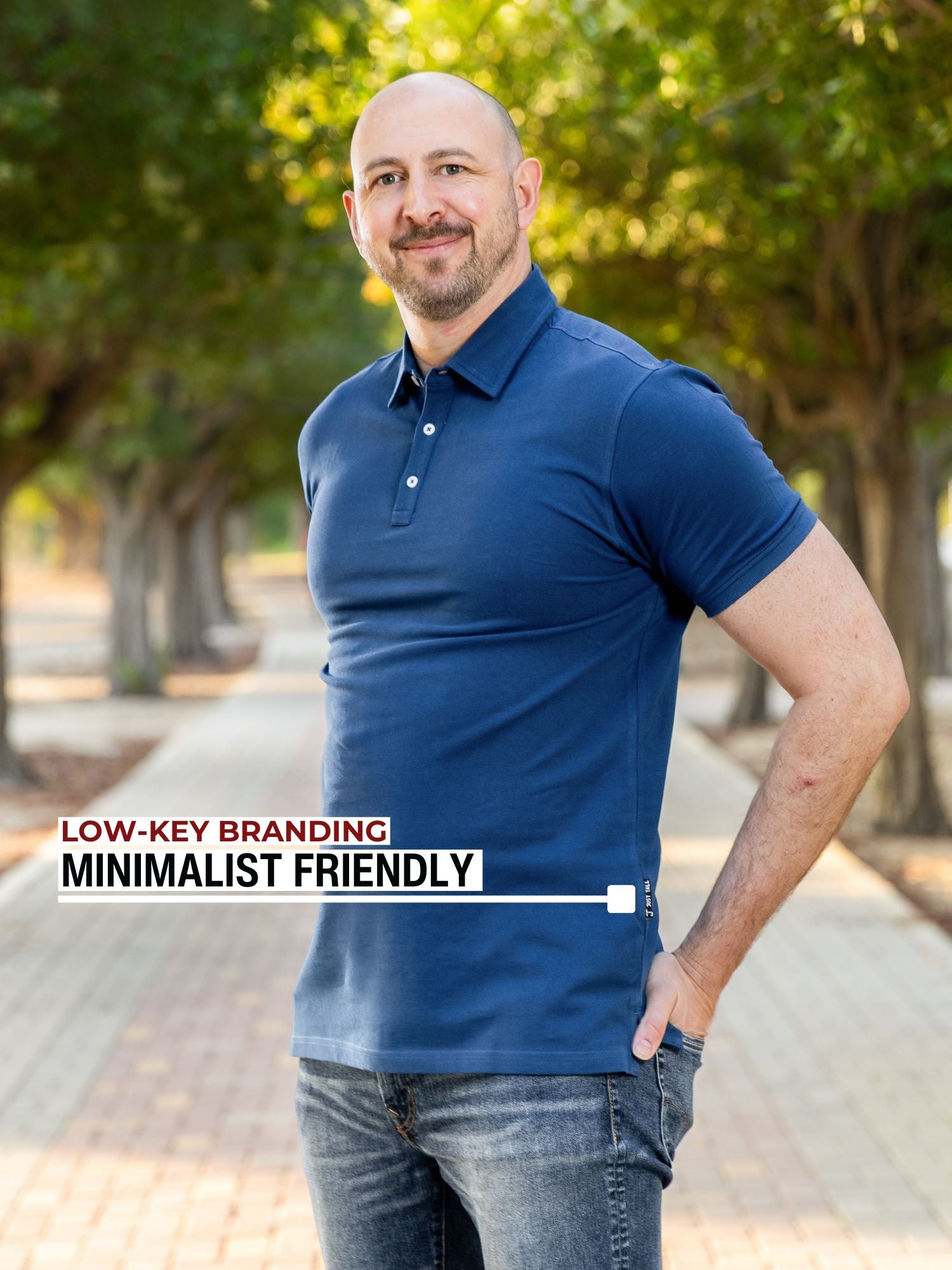 An upper body shot of a tall athletic guy in a park and wearing an XL tall slim navy polo shirt and showing the minimal Just Tall flag logo near the bottom of the side seam.