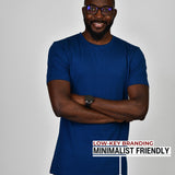A tall slim guy standing in a studio and wearing a navy large tall t-shirt, smiling and arms folded.