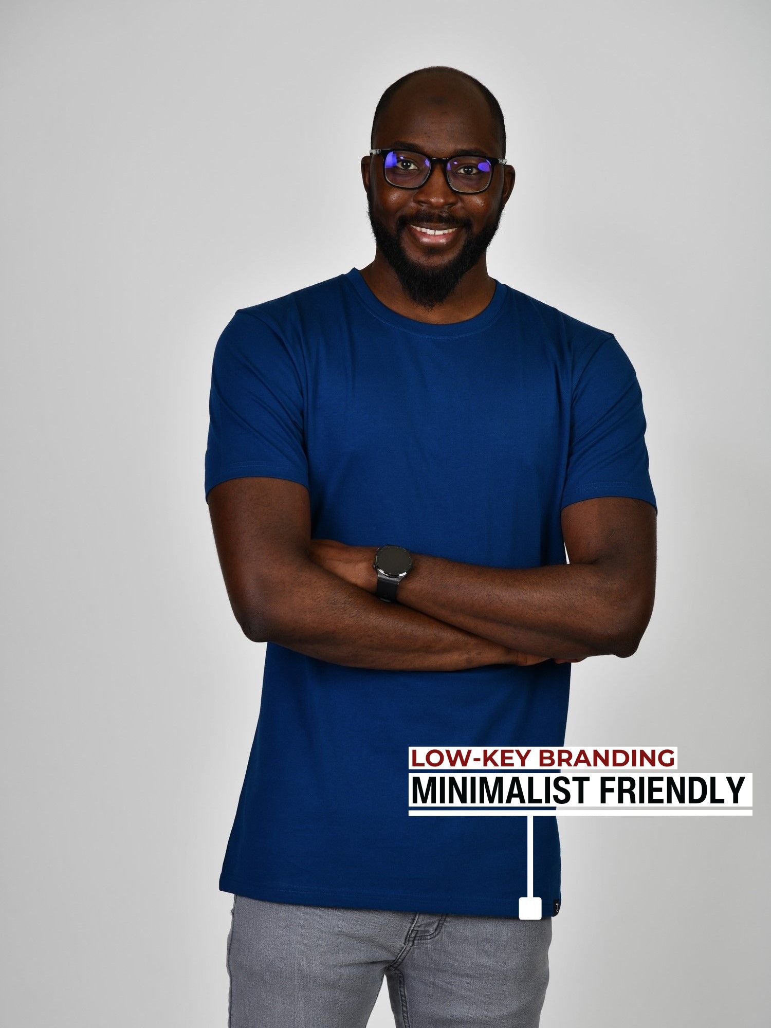 A tall slim guy standing in a studio and wearing a navy large tall t-shirt, smiling and arms folded.