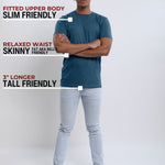 A head to toe shot of a tall slim guy  in a studio and wearing a petrol medium tall slim t-shirt, arms folded.
