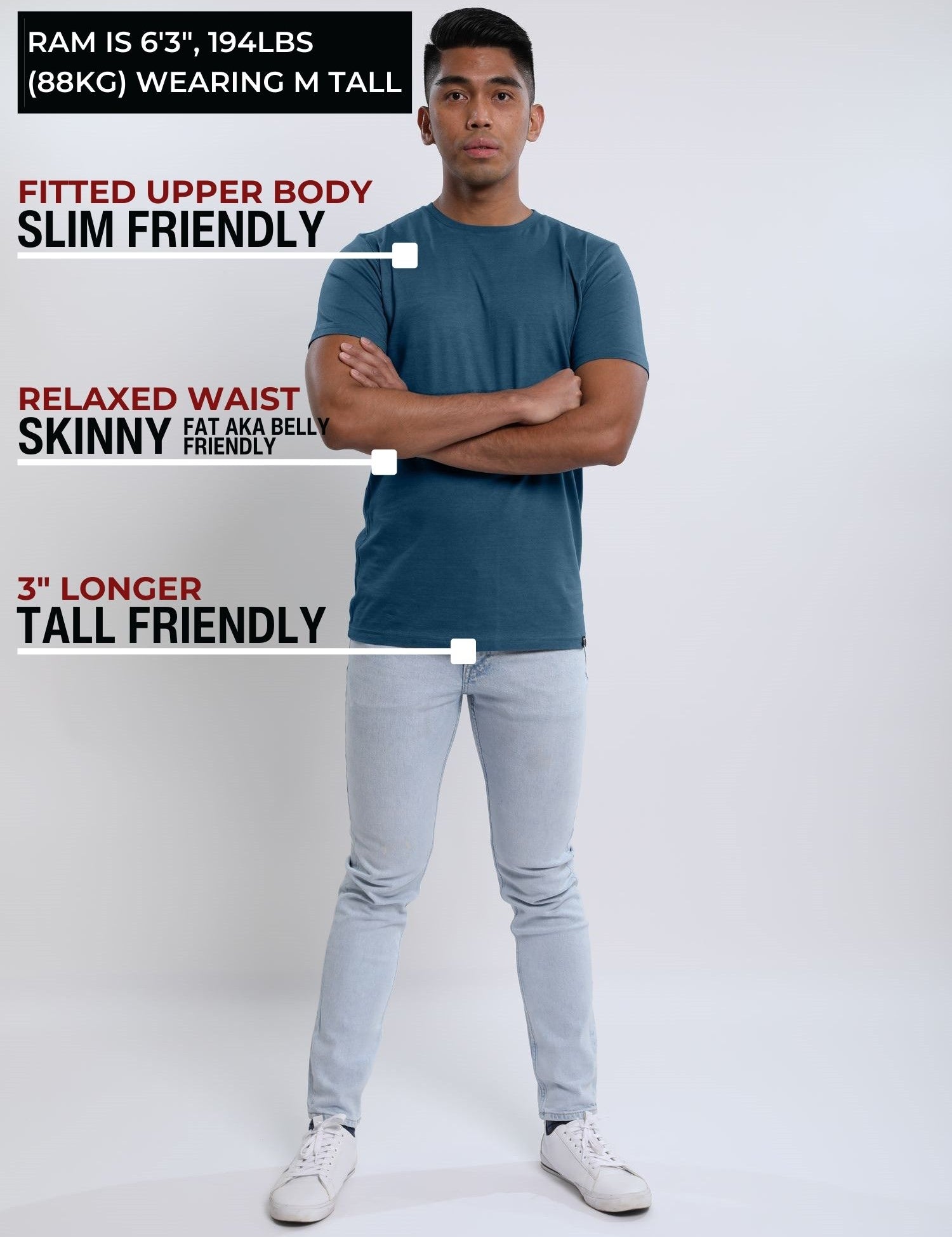 A head to toe shot of a tall slim guy  in a studio and wearing a petrol medium tall slim t-shirt, arms folded.