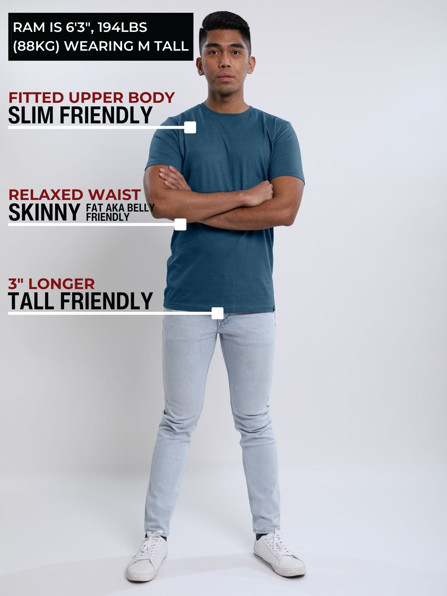 A head to toe shot of a tall slim guy in a studio and wearing a petrol medium tall slim t-shirt, arms folded.