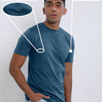 An upper body shot of a tall slim guy in a studio and wearing a petrol medium tall t-shirt, hand in pocket.