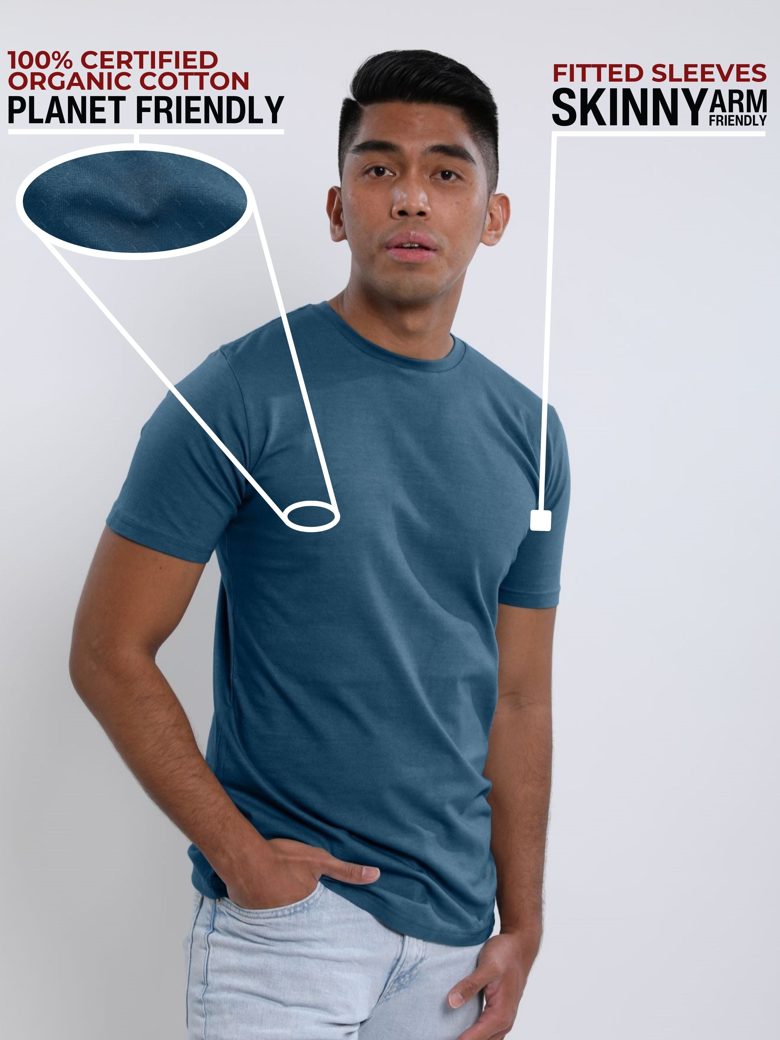 An upper body shot of a tall slim guy in a studio and wearing a petrol medium tall t-shirt, hand in pocket.