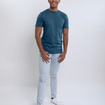 A head to toe shot of a tall slim guy  in a studio and wearing a petrol medium tall slim t-shirt.