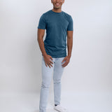 A head to toe shot of a tall slim guy in a studio and wearing a petrol medium tall slim t-shirt.