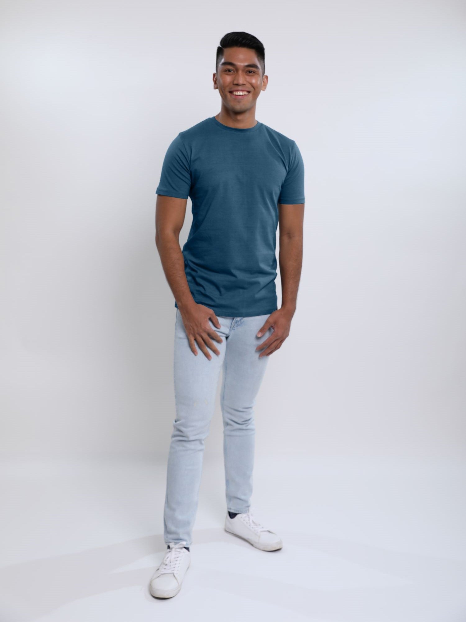 A head to toe shot of a tall slim guy in a studio and wearing a petrol medium tall slim t-shirt.