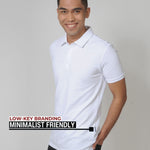 An upper body shot of a tall slim guy in a studio and wearing a medium tall slim white polo shirt and showing the minimal Just Tall flag logo near the bottom of the side seam.