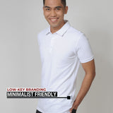 An upper body shot of a tall slim guy in a studio and wearing a medium tall slim white polo shirt and showing the minimal Just Tall flag logo near the bottom of the side seam.