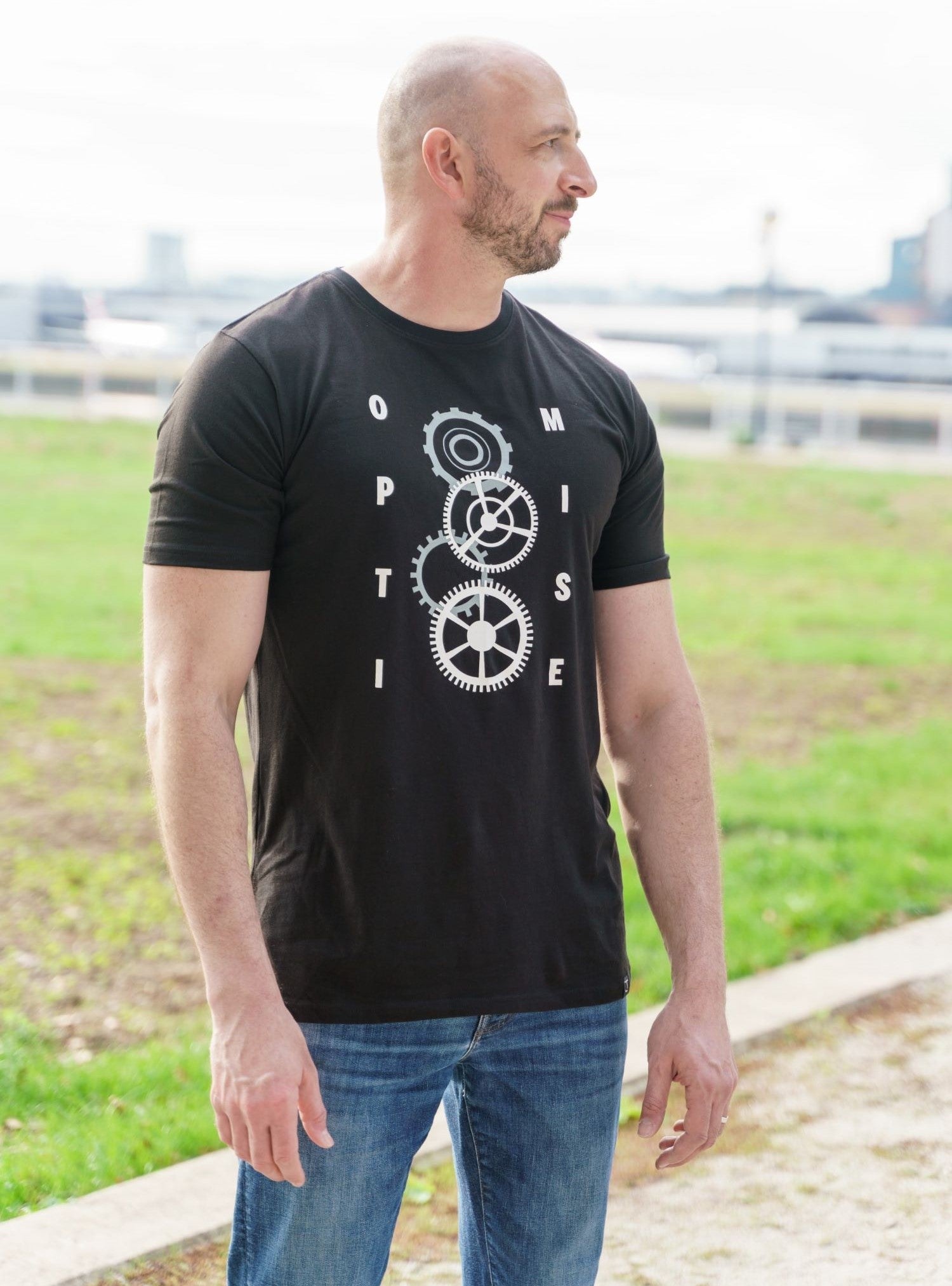 A tall slim guy wearing a black tall graphic t-shirt in a park.