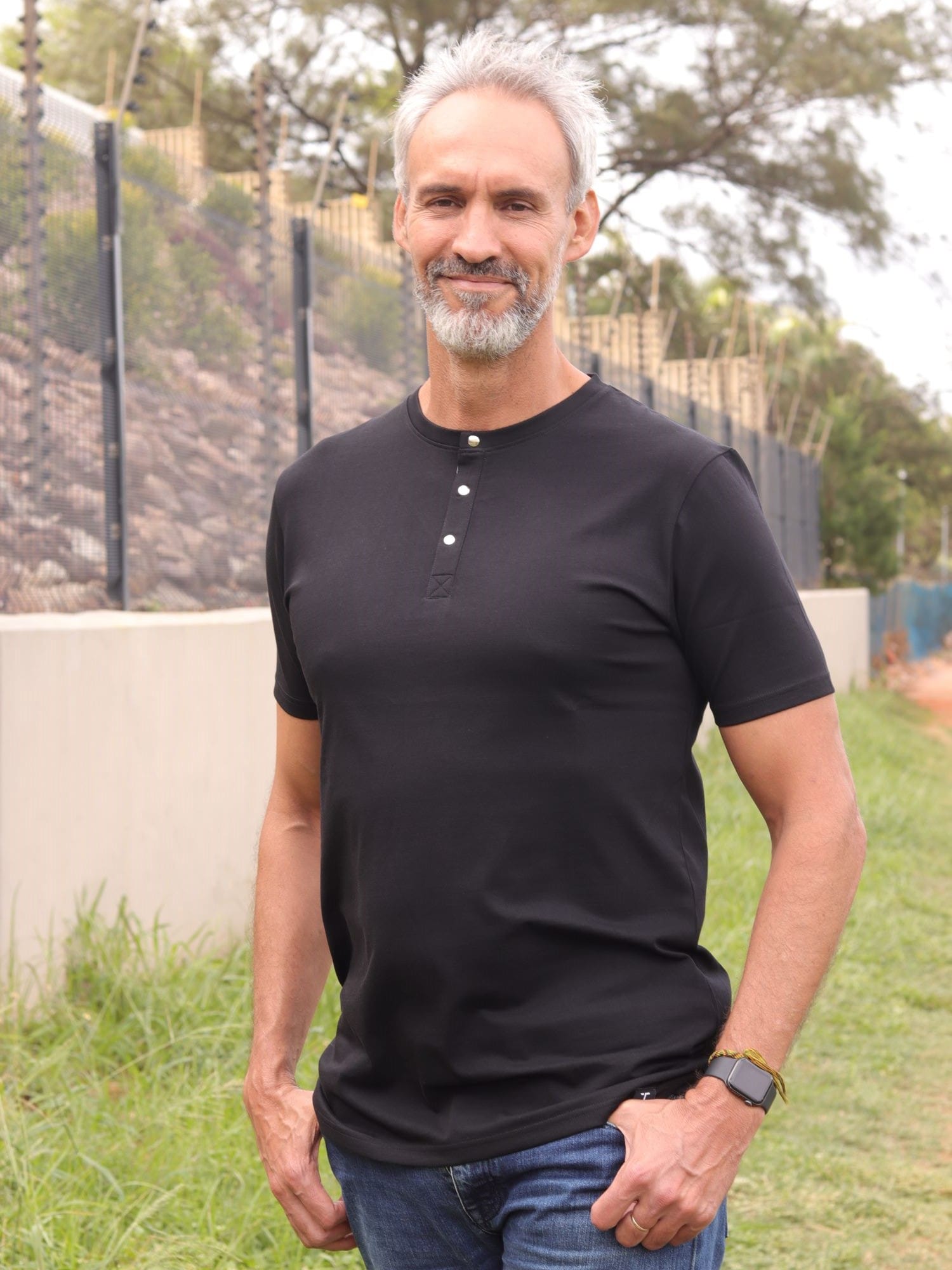A tall skinny guy wearing a tall black henley shirt and smiling.