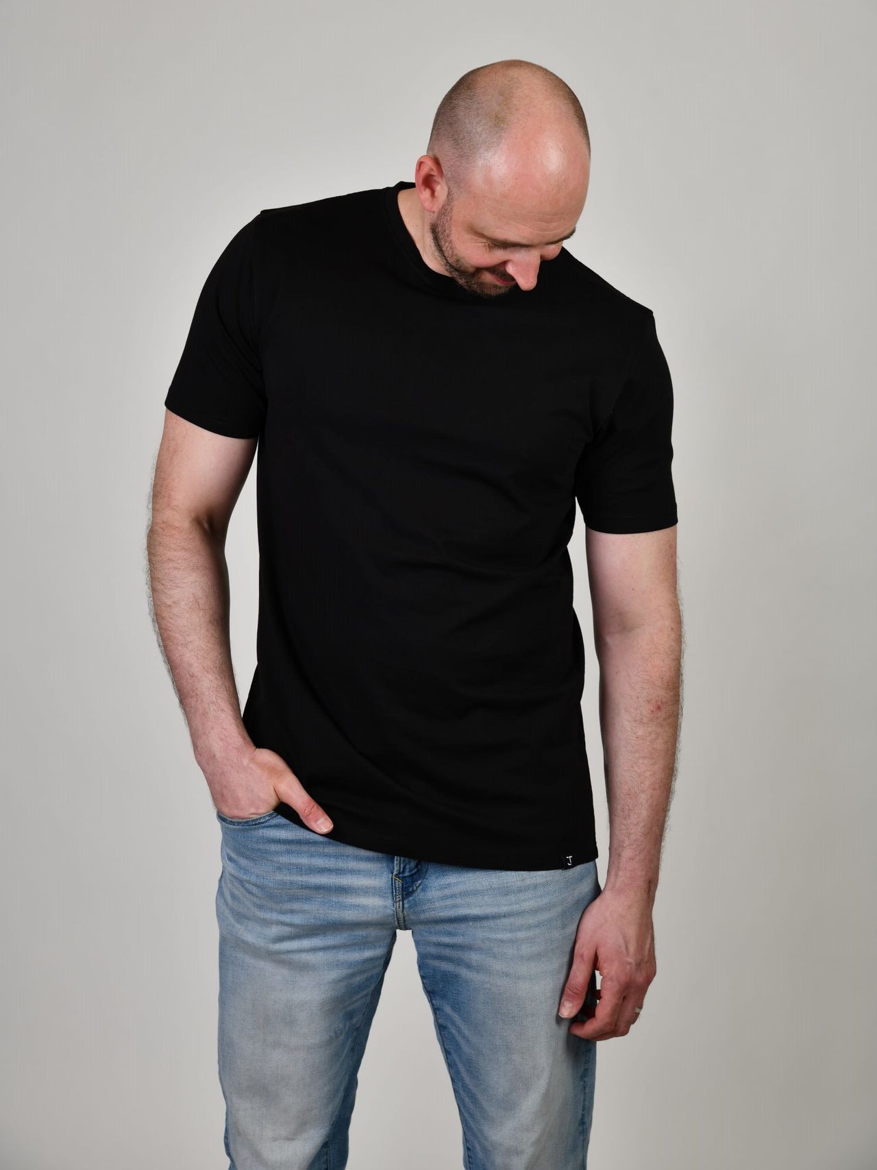 A tall and slim guy smiling in the studio and wearing a black XL tall slim t-shirt.