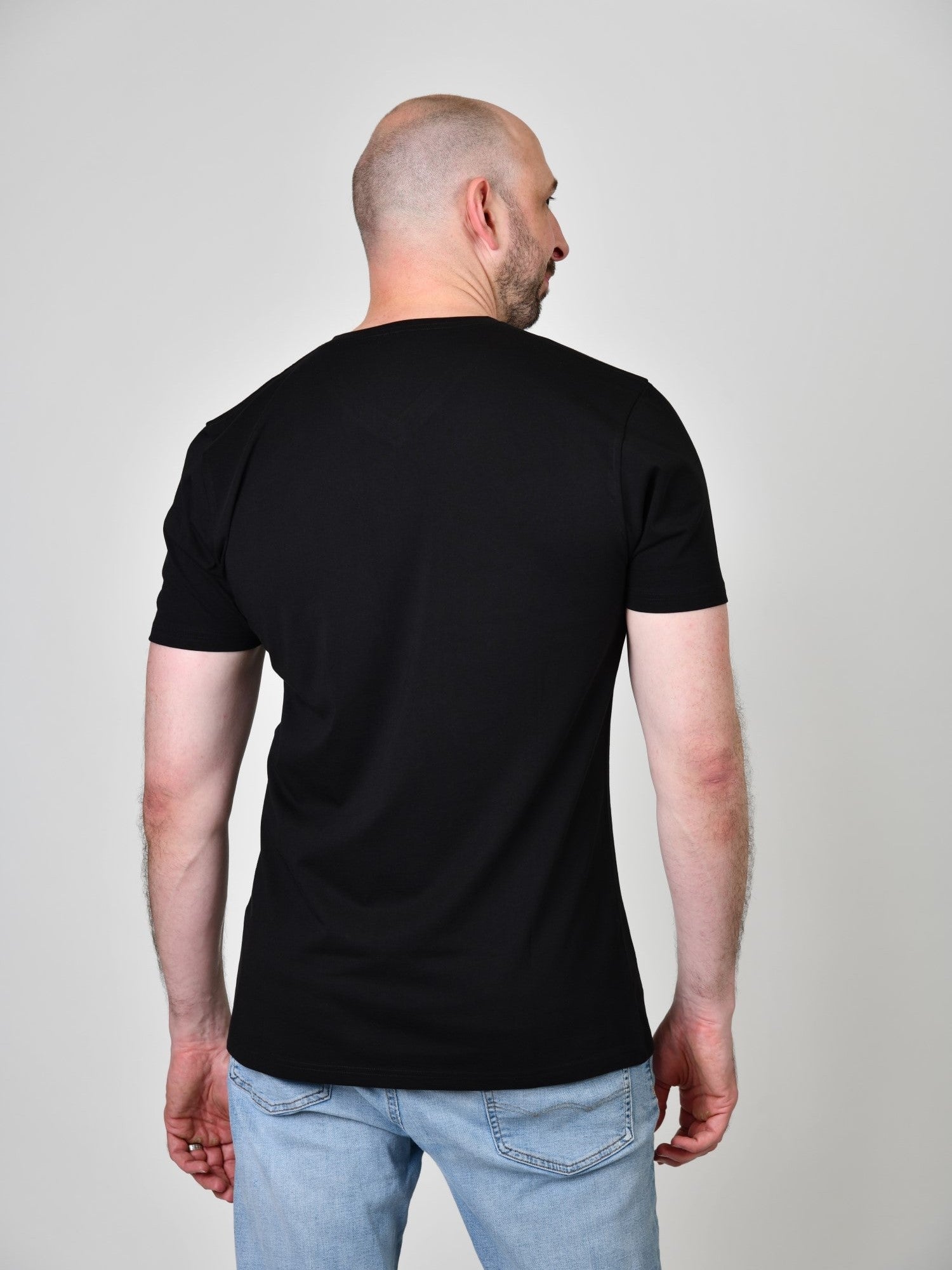 A shot from behind of a tall and slim guy in the studio and wearing a black XL tall slim v-neck t-shirt.