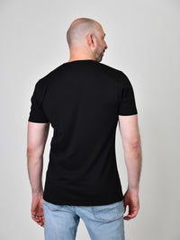 Thumbnail for A shot from behind of a tall and slim guy in the studio and wearing a black XL tall slim v-neck t-shirt.