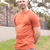 A tall slim guy, hands behind back, wearing a brown XL tall henley shirt.