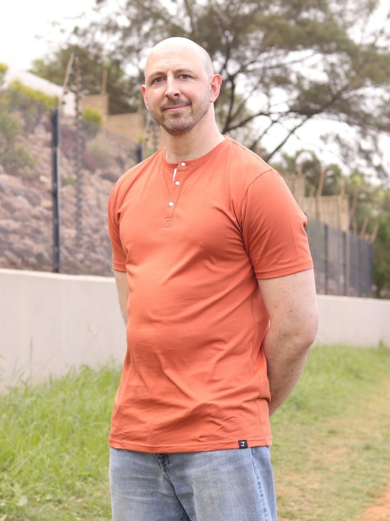 A tall slim guy, hands behind back, wearing a brown XL tall henley shirt.