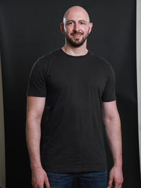 Thumbnail for A tall and slim guy smiling in the studio and wearing a charcoal XL tall slim t-shirt.