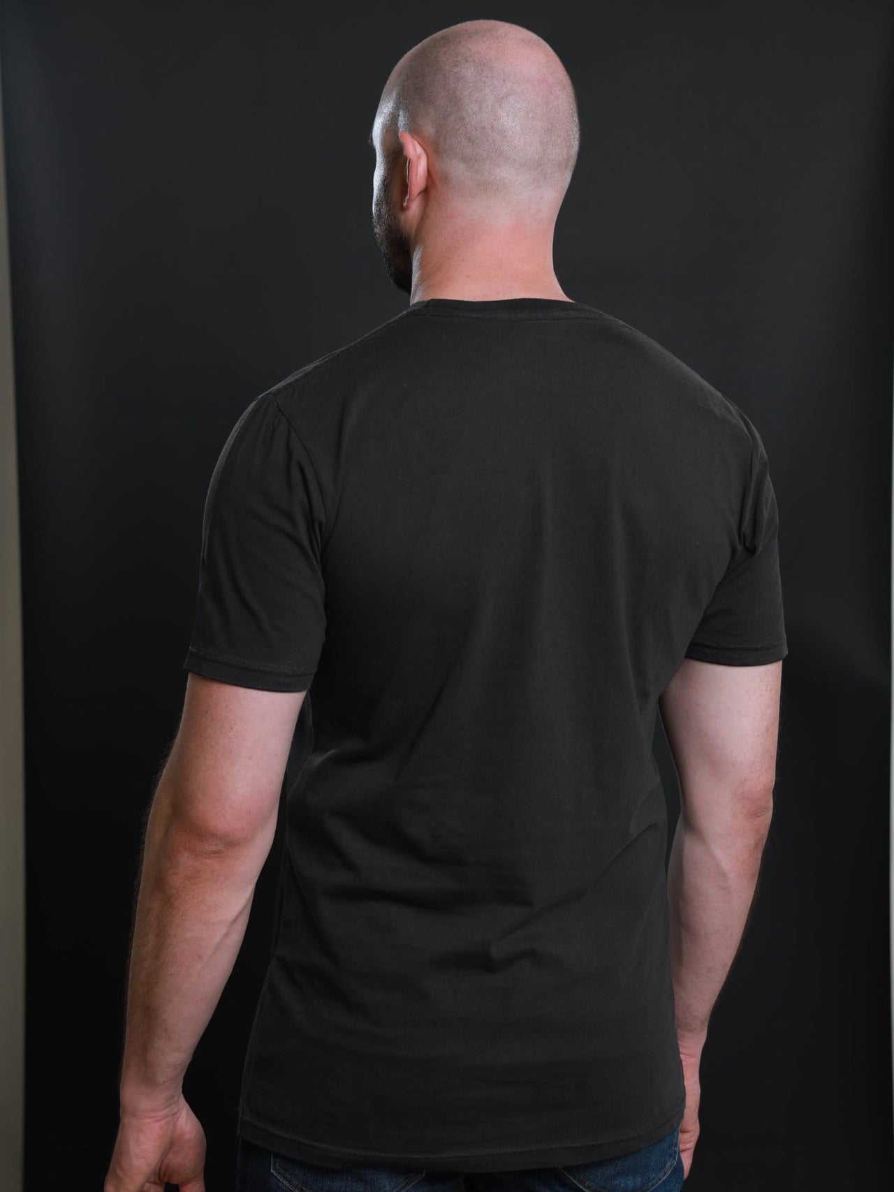 A shot from behind of a tall and slim guy in the studio and wearing a charcoal XL tall slim t-shirt.