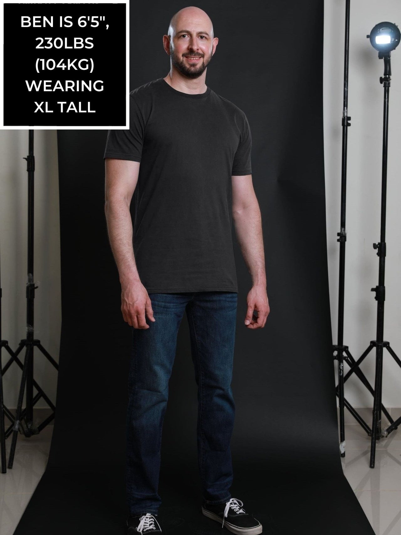 A head to toe shot of a tall and slim guy in the studio wearing a charcoal XL tall slim t-shirt.
