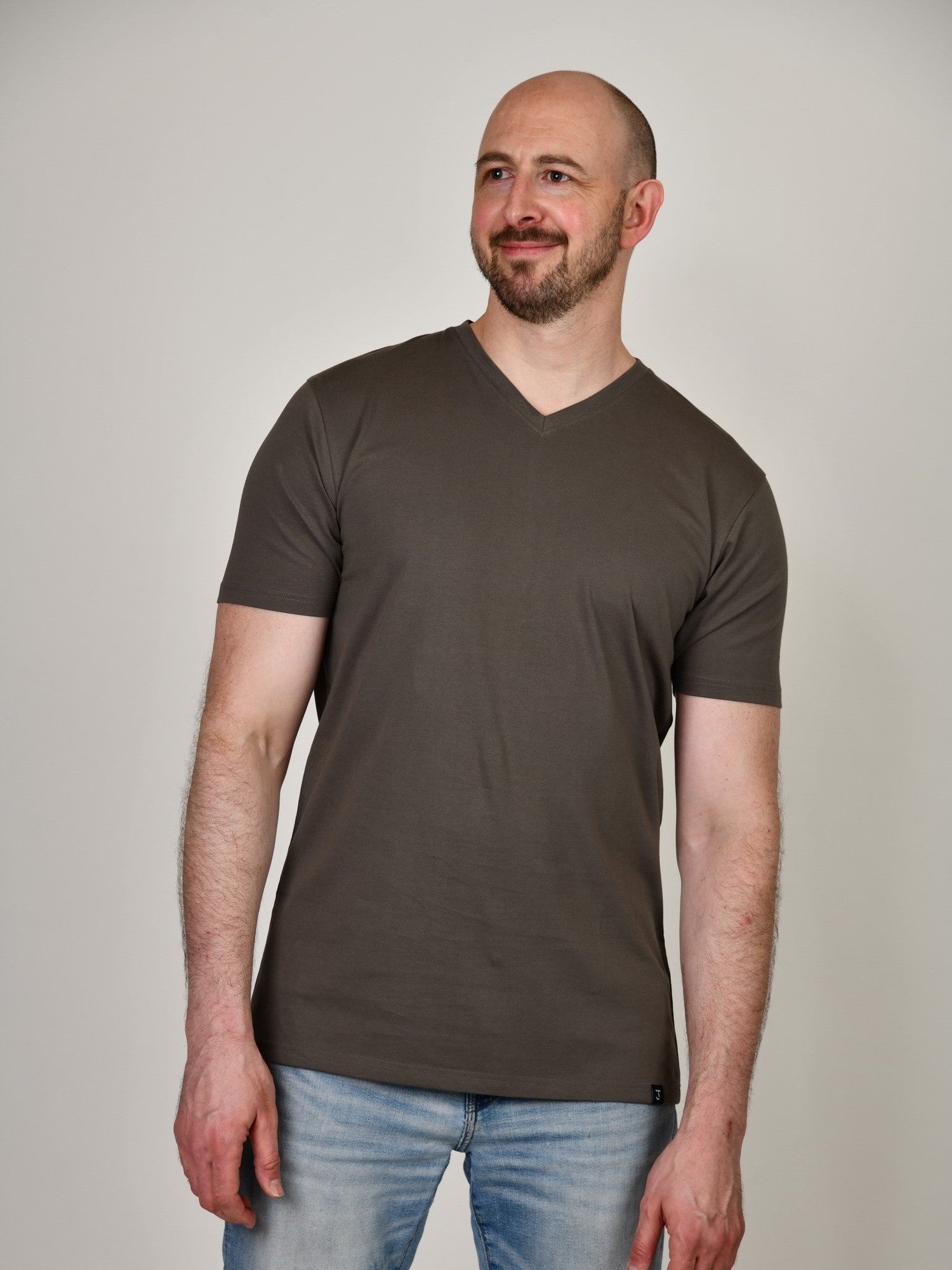 A tall and slim guy smiling in the studio and wearing a dark grey XL tall slim v-neck t-shirt.