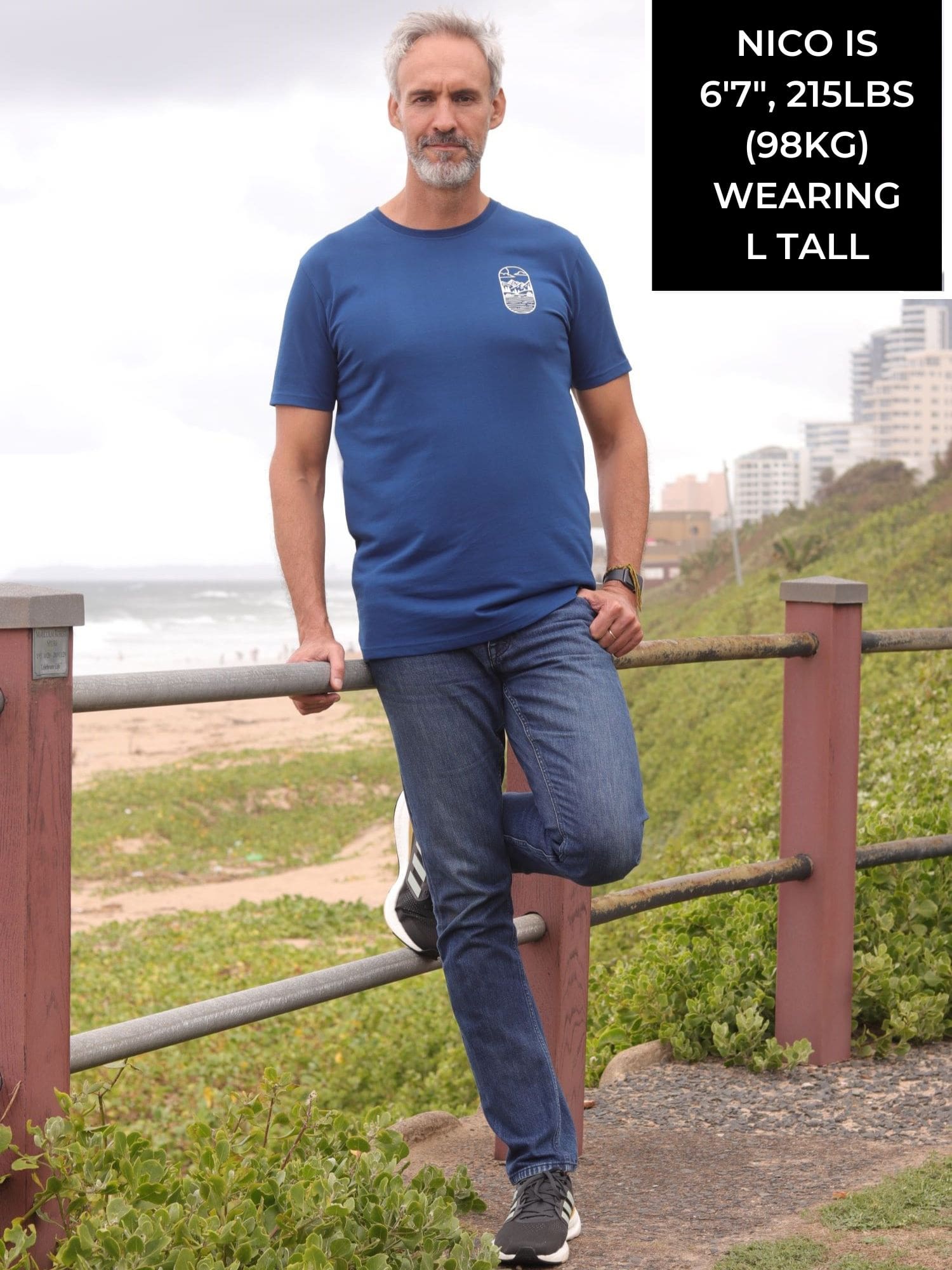A head to toe shot of a tall slim guy in an L tall graphic t-shirt with a lake design.