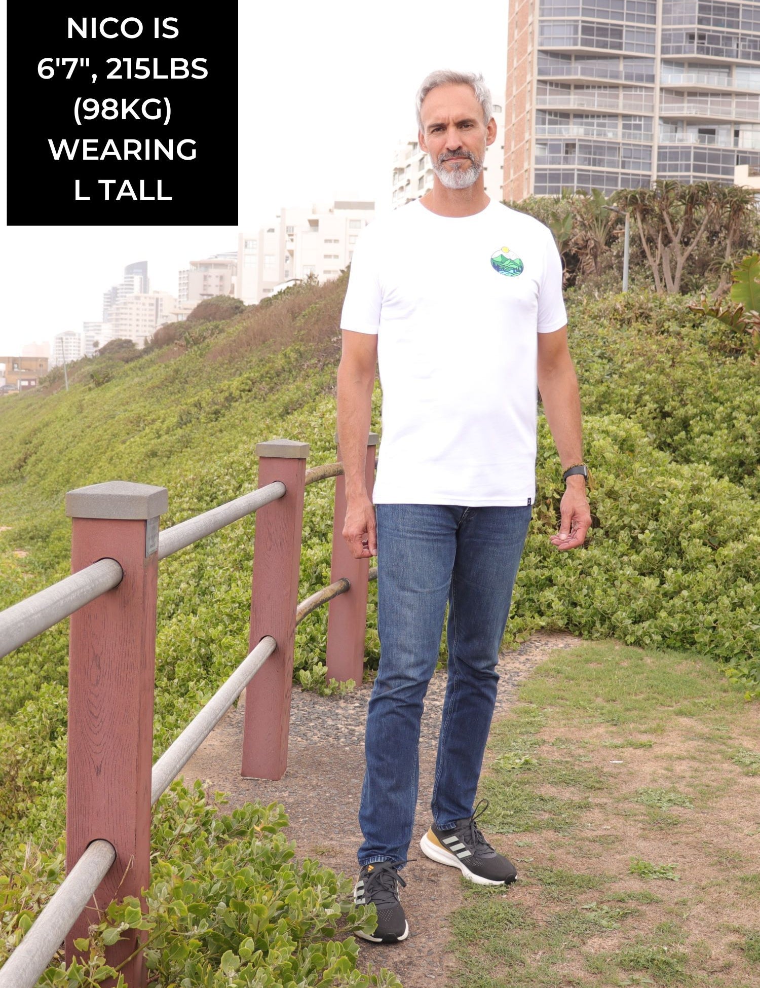 A head to toe shot of a tall slim guy in an L tall graphic t-shirt with a landscape design.