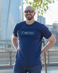 Thumbnail for A tall and slim guy in the street with his hands behind his back and wearing a navy blue Just Tall branded graphic tall t-shirt.