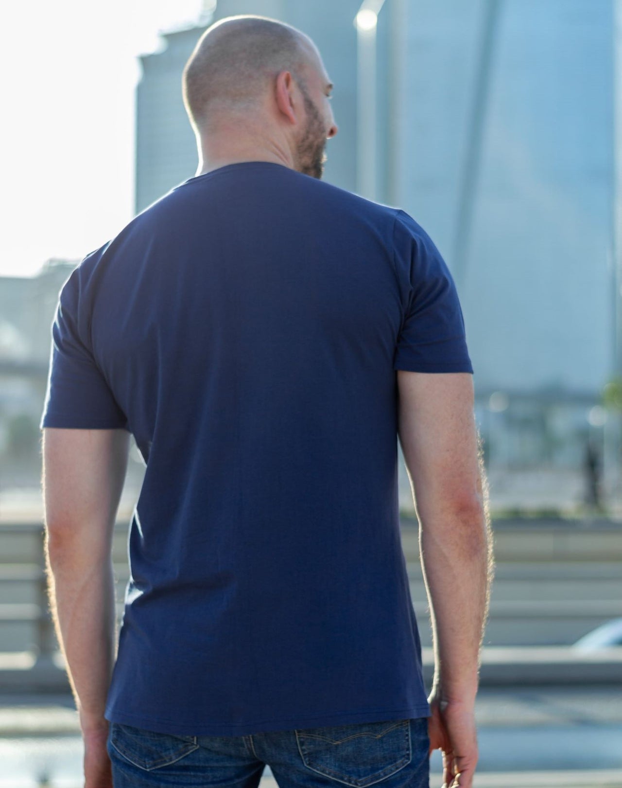 A shot from behind of a tall slim guy in the street and wearing a navy blue tall slim fit t-shirt.