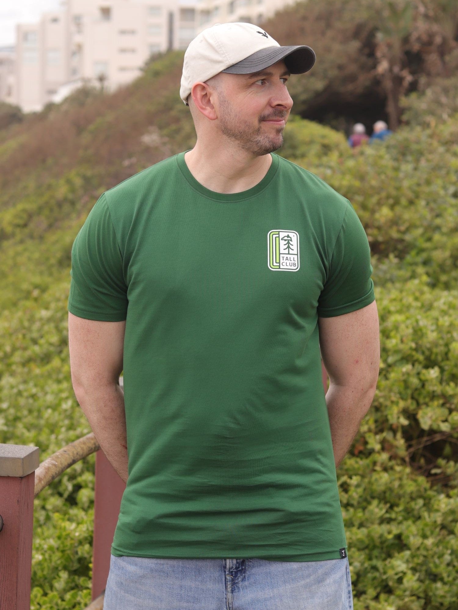 An upper body shot of a tall slim guy in an XL tall graphic t-shirt with a tall club design, hands behind back.