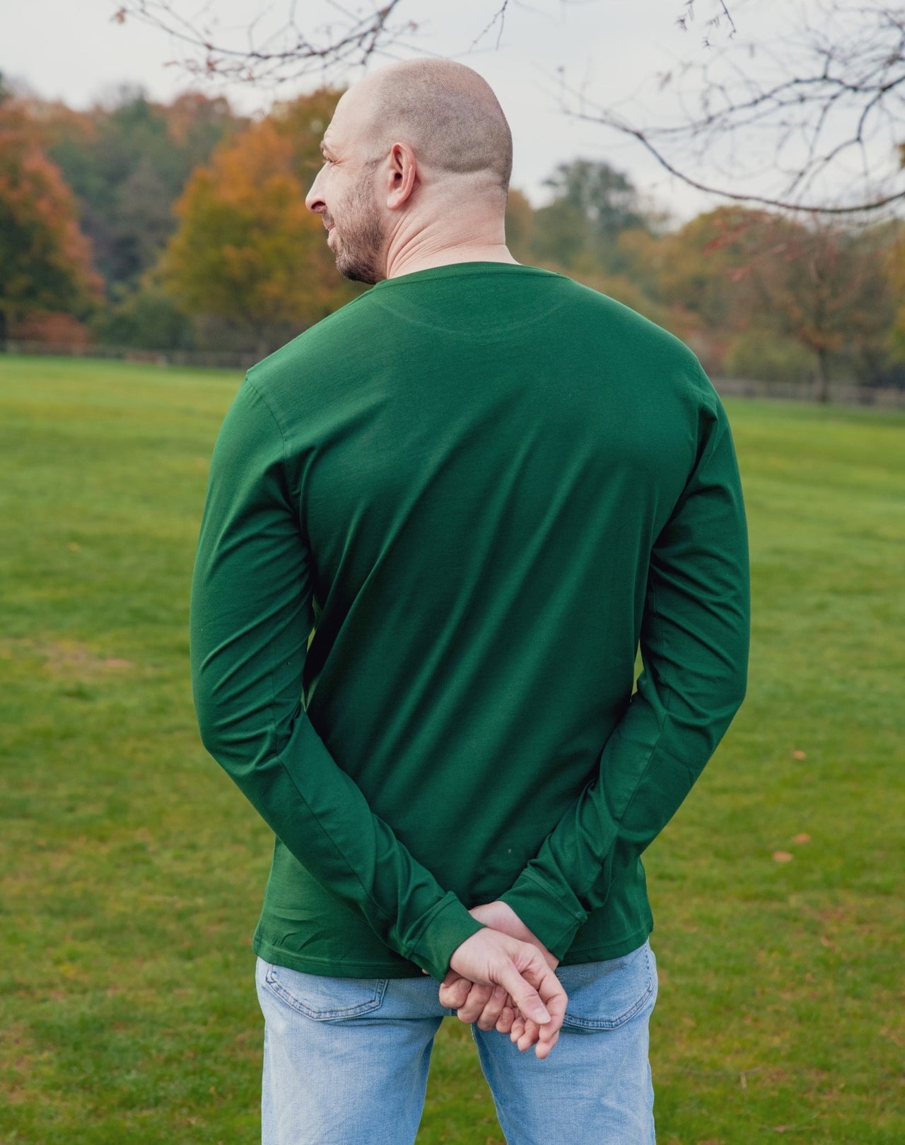 A shot from behind of a tall athletic guy wearing a long sleeve dark green tall t-shirt, hands crossed behind his back.