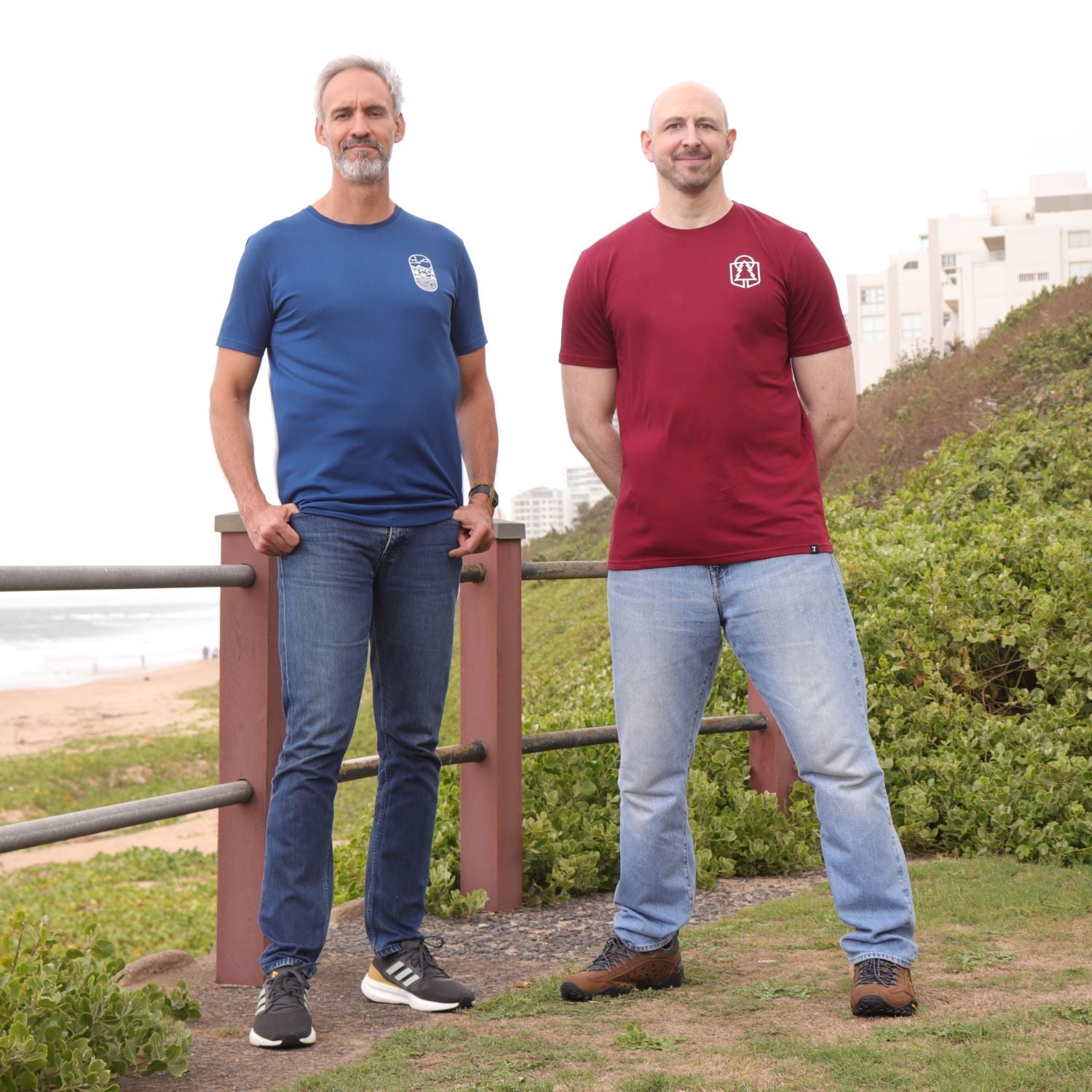 Two tall slim men standing at the coastline and wearing navy and maroon tall slim graphic t-shirts.