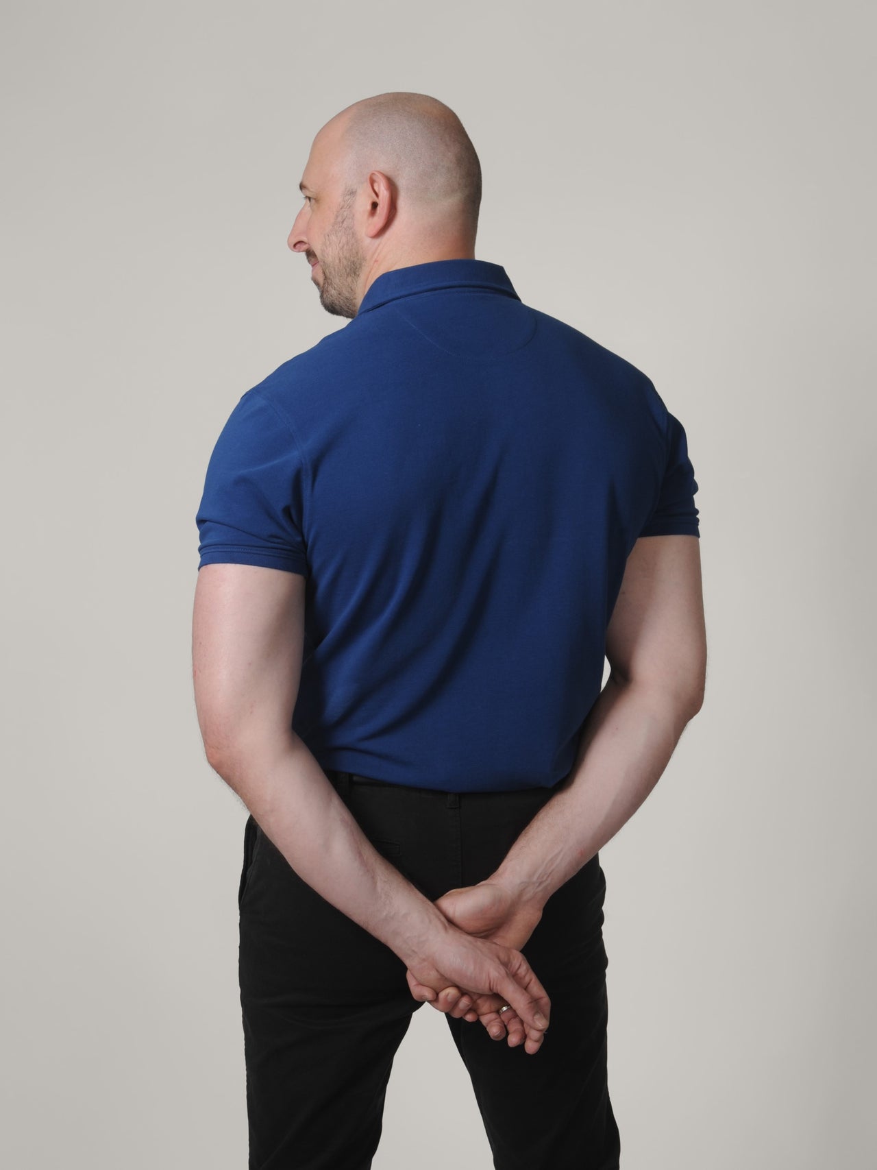 A shot from behind of a tall skinny guy wearing a XL tall navy pique polo shirt.