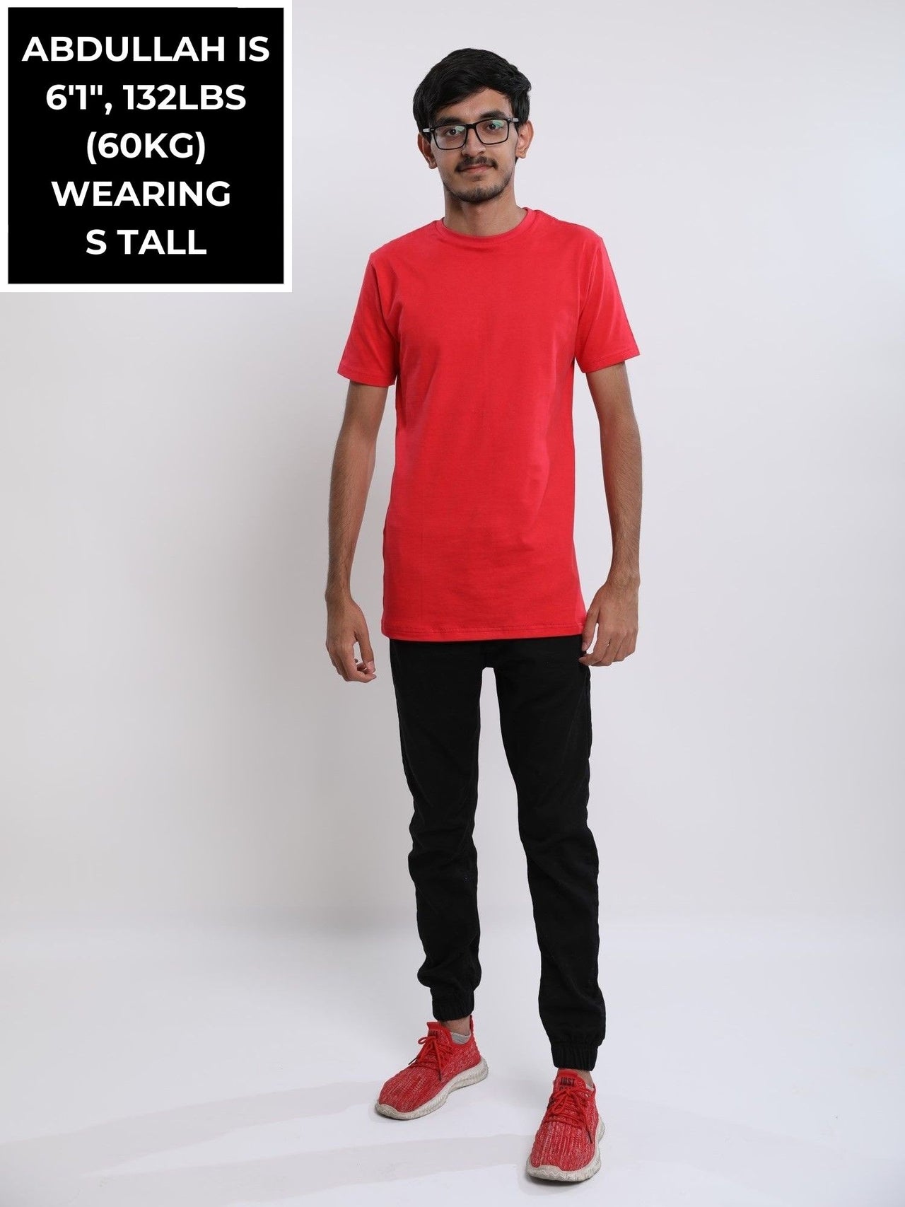 A head to toe shot of a tall skinny guy in the studio wearing a red small tall slim t-shirt.