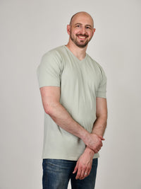 Thumbnail for A tall and slim guy smiling in the studio, one hand grasping the other arm and wearing a sage green XL tall slim v-neck t-shirt.