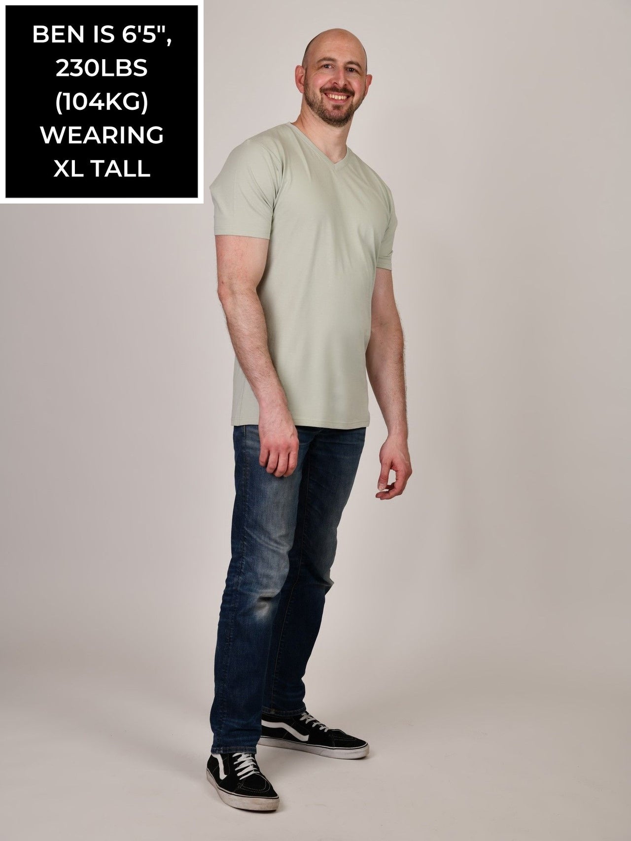 A head to toe shot of a tall and slim guy in the studio wearing an XL tall sage green slim v-neck t-shirt.