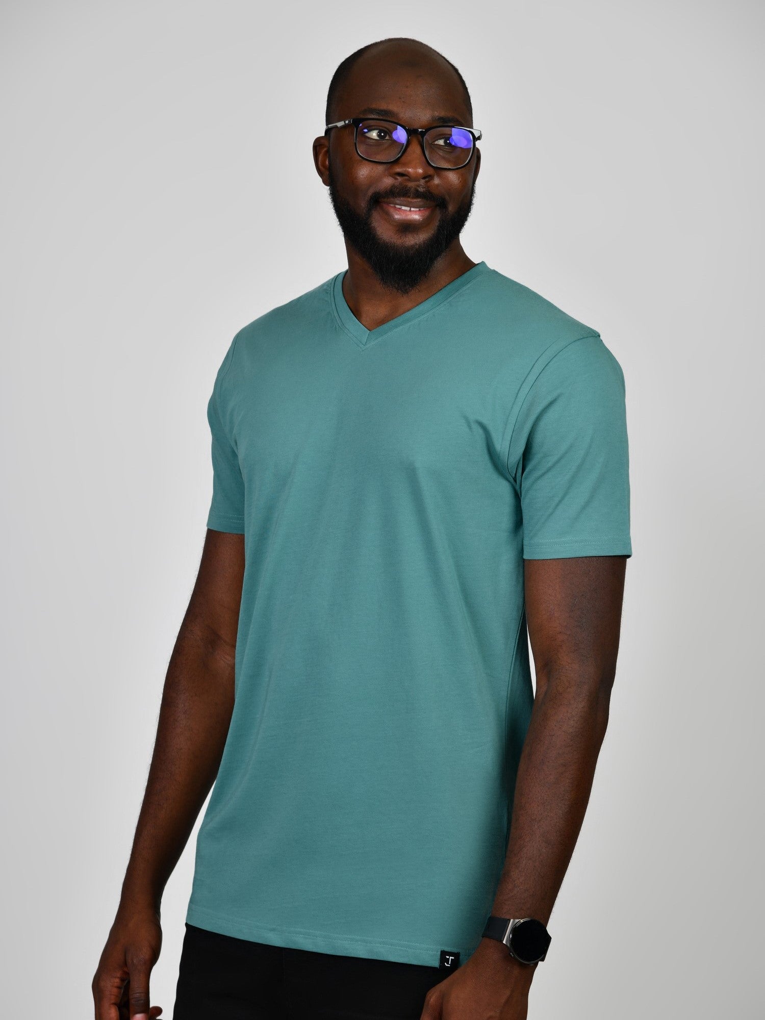 A tall and slim guy smiling in the studio and wearing a teal L tall slim v-neck t-shirt.