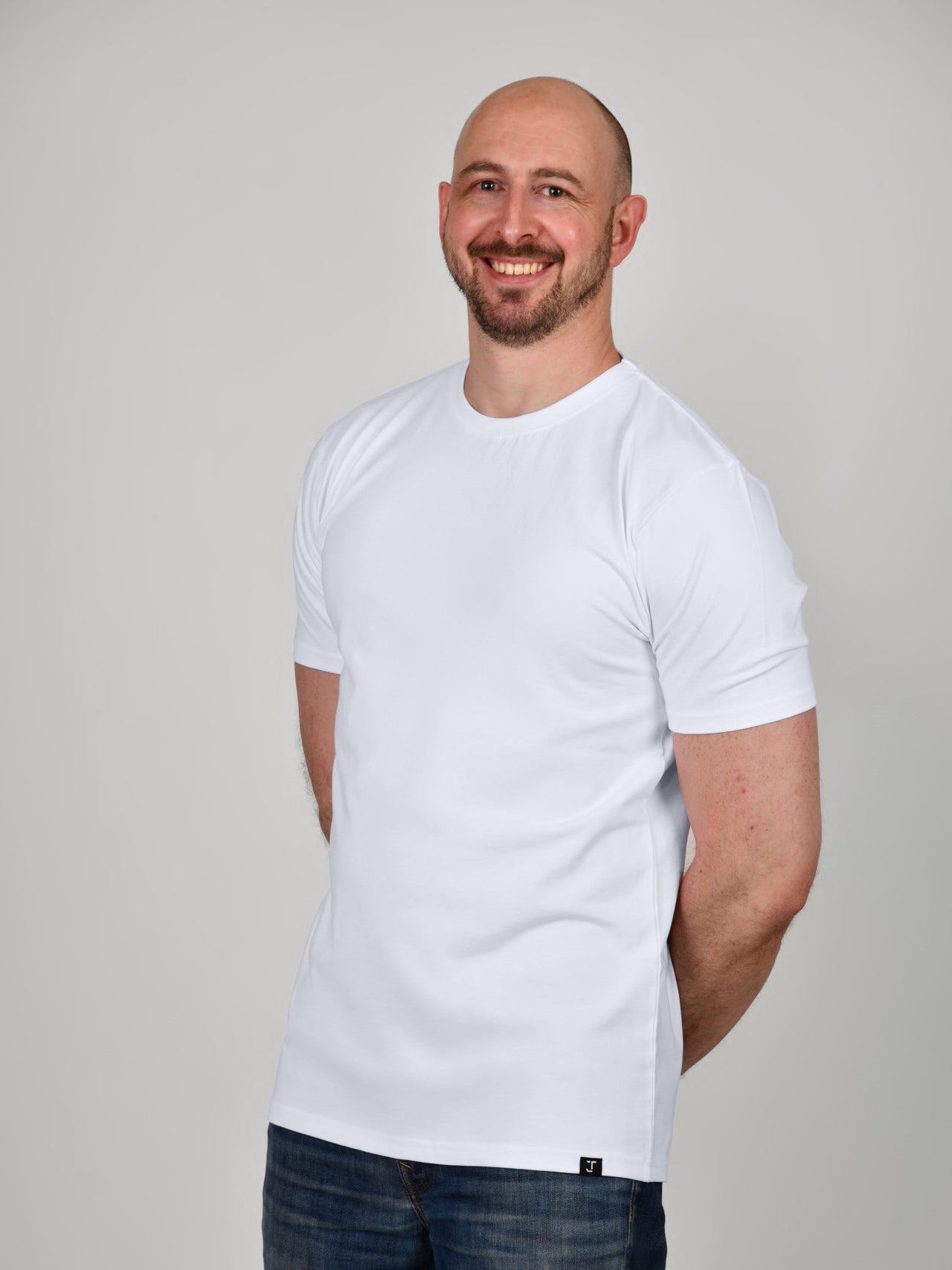 A tall and slim guy in the studio, hands behind back and wearing a white XL tall slim fit t-shirt.