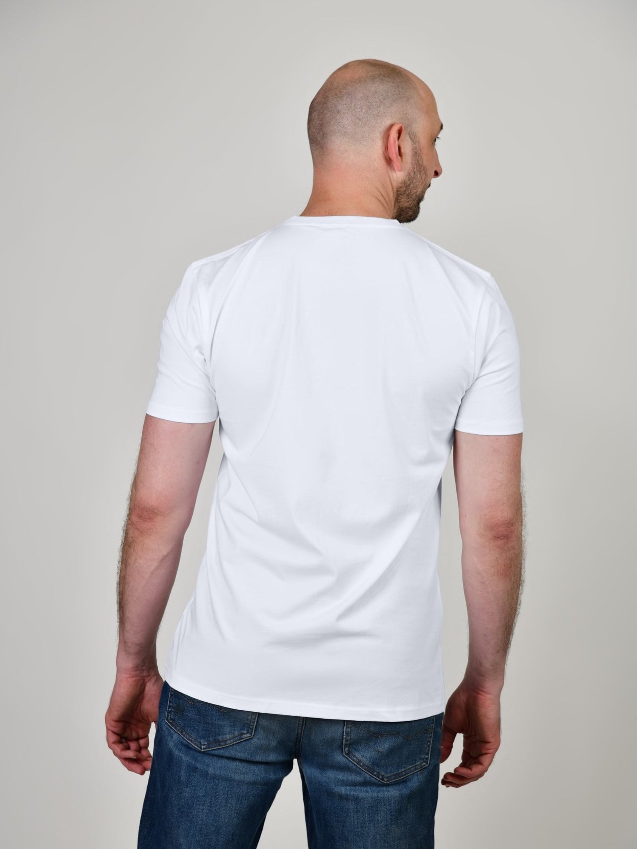 A shot from behind of a tall and slim guy in the studio and wearing a white XL tall slim t-shirt.