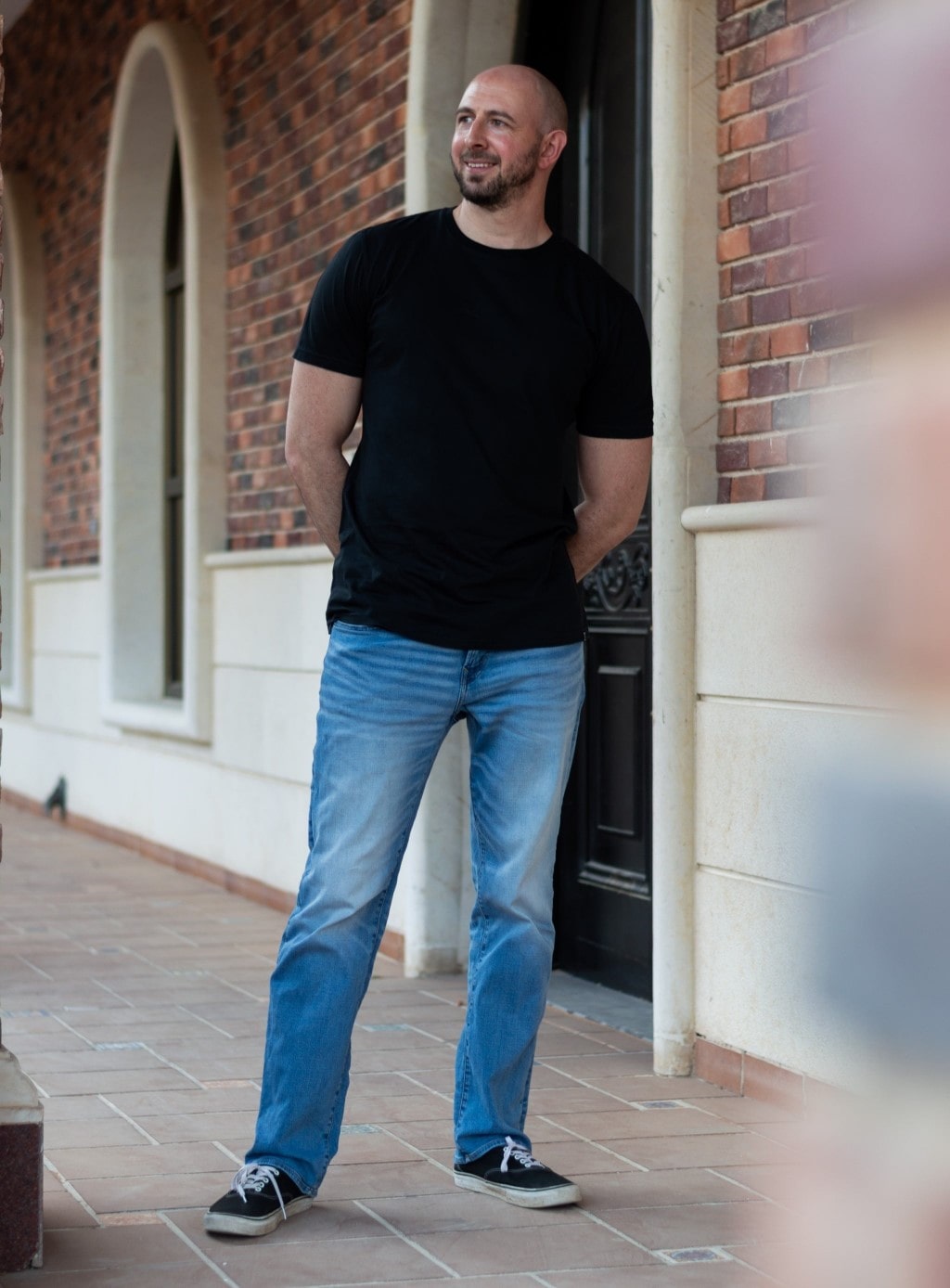 A tall skinny guy outside a house wearing a black tall slim t-shirt.