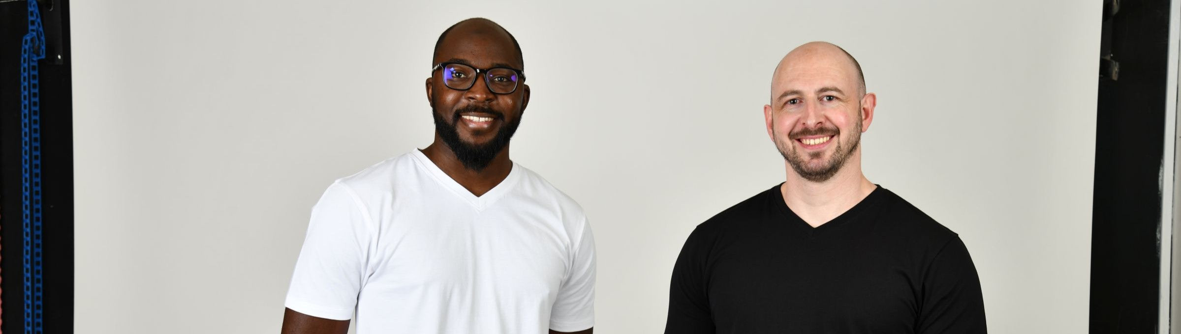 Two tall slim guys smiling in a studio and wearing black and white V-neck tall t-shirts.