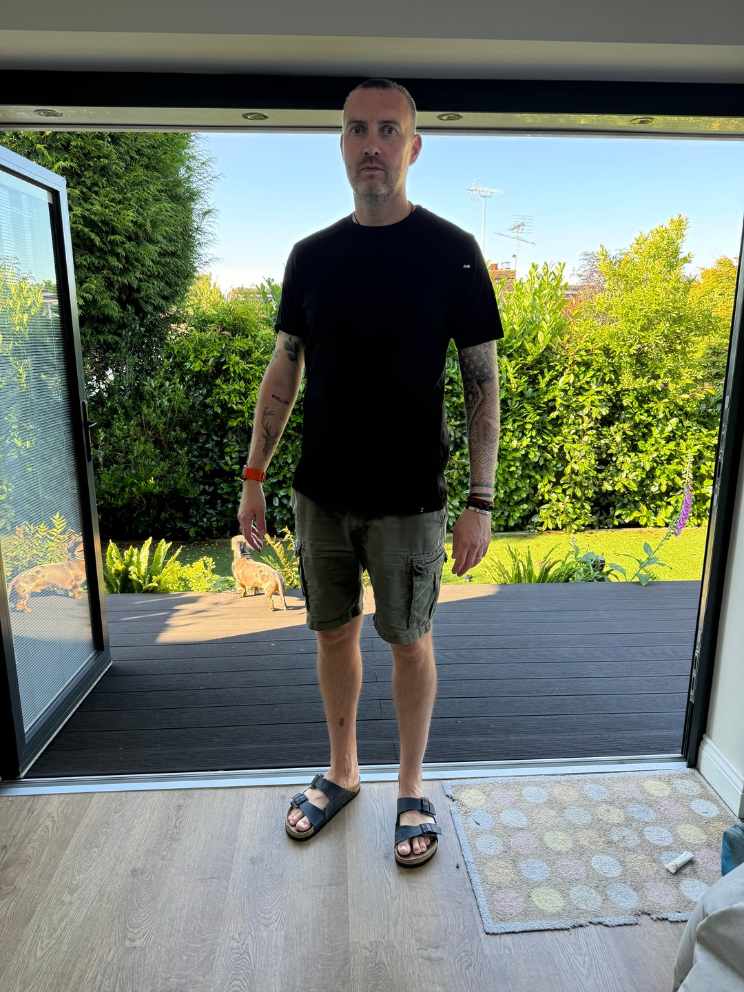 A tall slim guy wearing a black XL tall t-shirt in front of his garden patio.