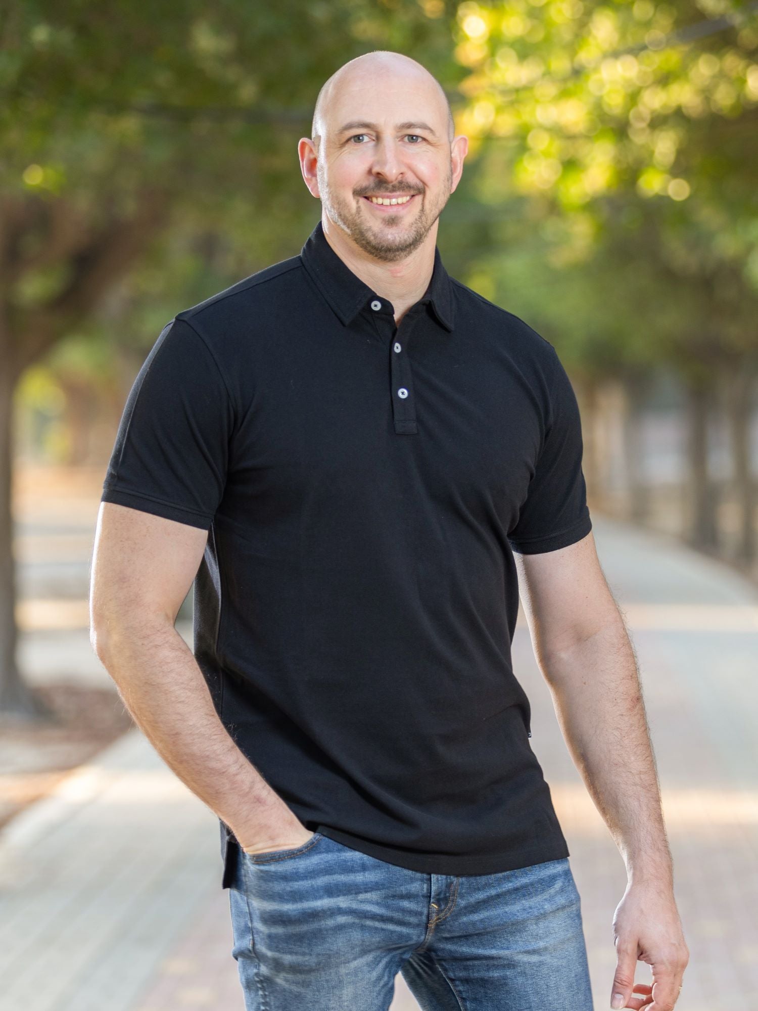 A tall athletic guy wearing an XL tall black polo shirt and standing in a park.