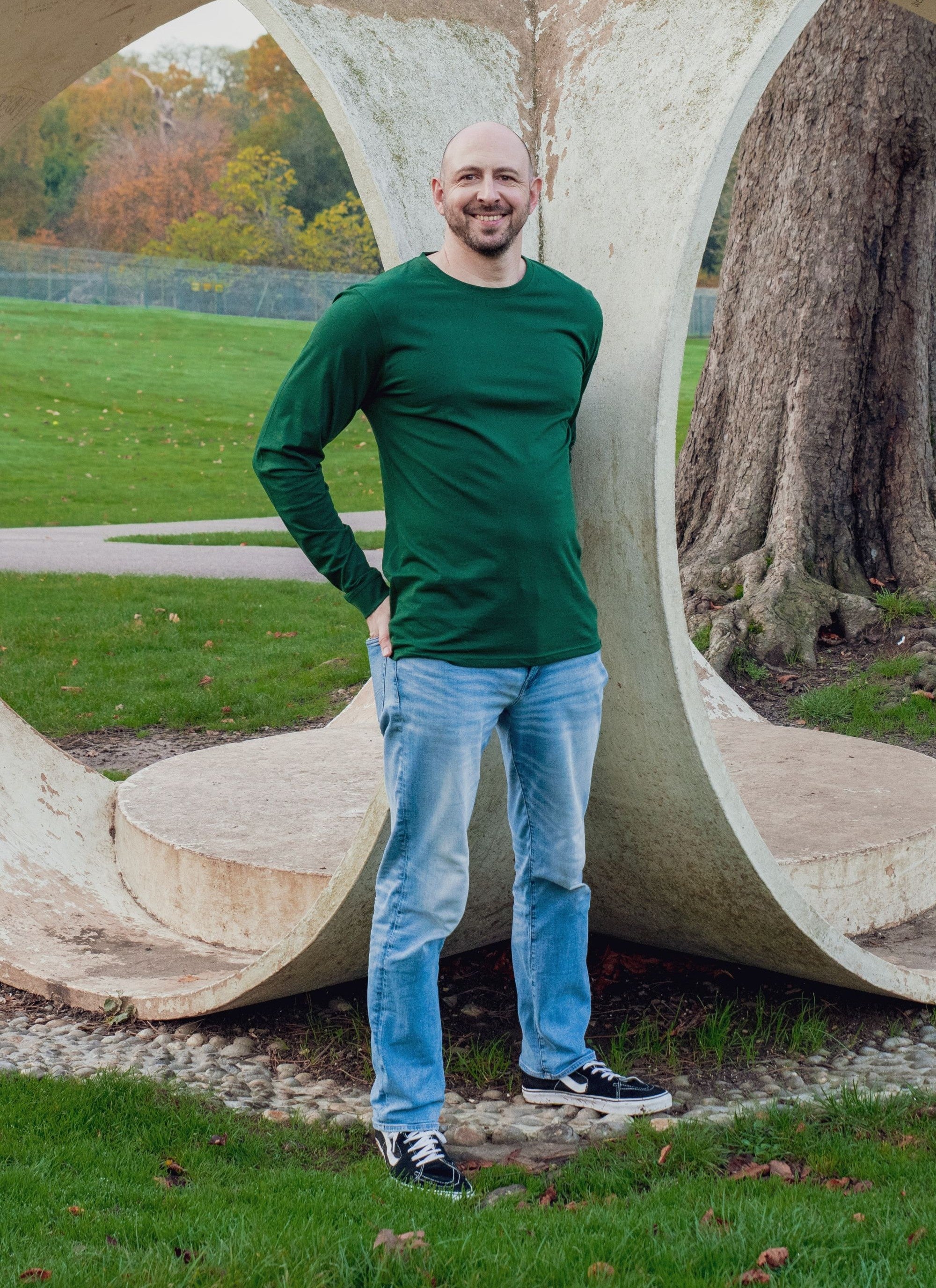 Ben Khalifa, the founder of Just Tall. He's wearing an extra long dark green long sleeve t-shirt. and standing in a park.