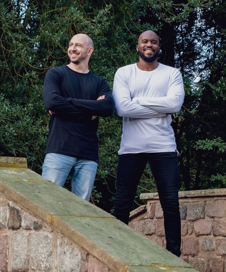 Two tall skinny guys on a bridge wearing black and white tall long sleeve t-shirts.