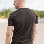 A shot from behind of a tall skinny guy wearing a tall black graphic t-shirt.