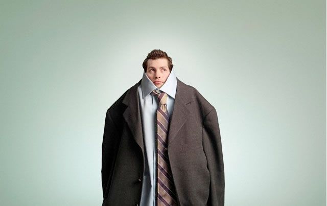 A funny photo of a guy wearing a huge baggy suit, only his face poking out of the top of the suit.