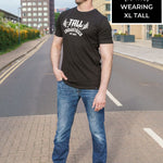 A head to toe shot of a tall skinny guy wearing a tall graphic bodybuilding t-shirt.