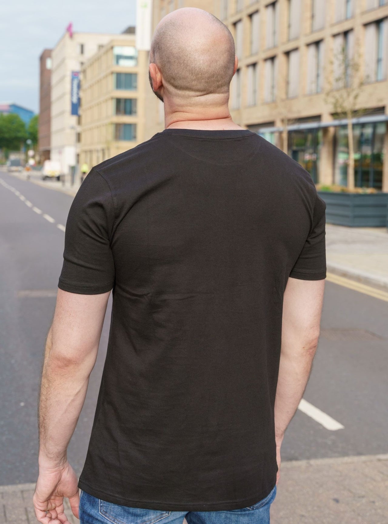 A shot from behind of a tall skinny guy wearing a tall slim graphic t-shirt.