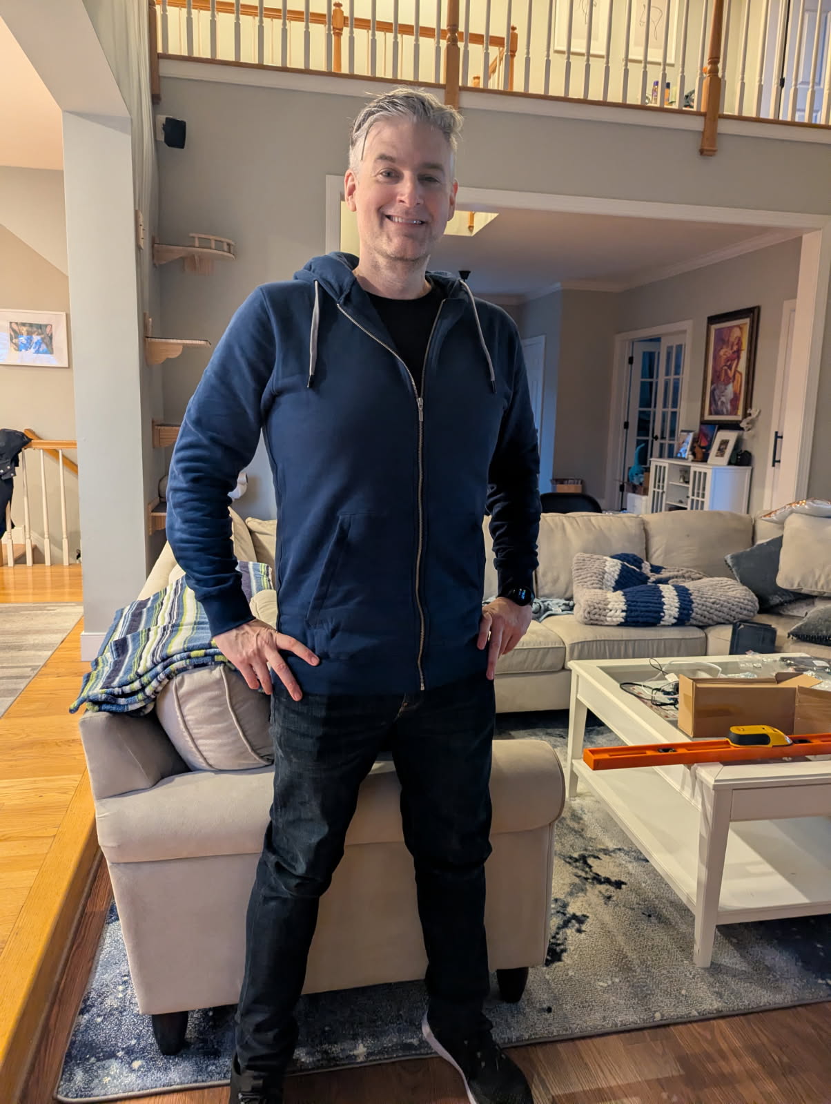 Tall slim man wearing a navy hoodie in a living room.